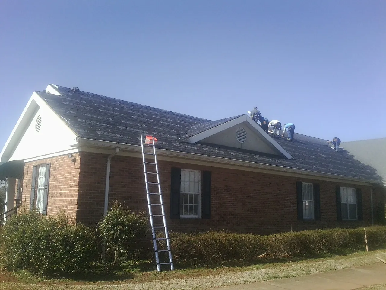 Crew tearing shingles off a brick ranch roof with a ladder set — Metal Roof Repair work by our crew in Wrentham