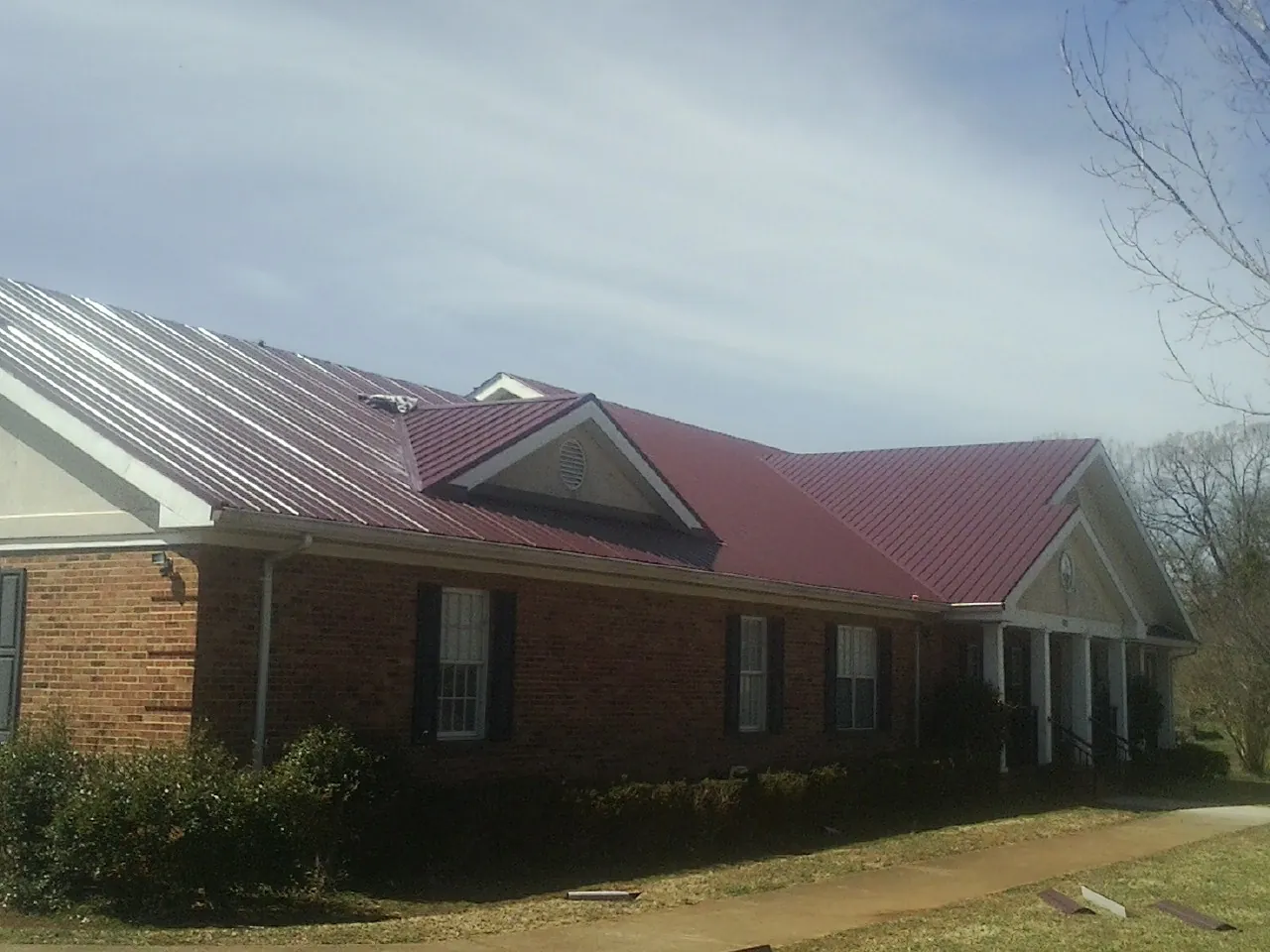 Red metal roof with gabled entries on a long brick building, from a Hail Damage Roof Repair job in Wrentham