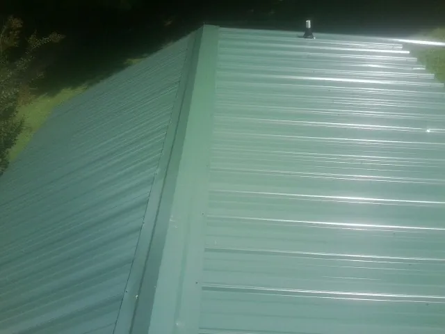 New green metal panels meeting at the ridge of a roof — Flat Roof Repair work by our crew in Wrentham