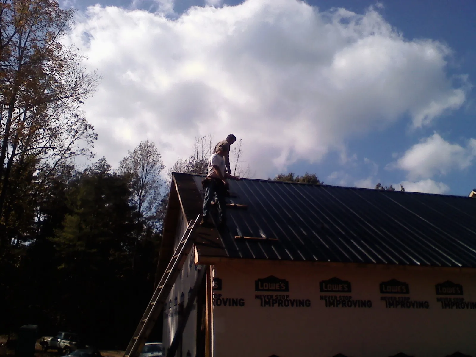 Roofer fastening dark metal panels high against a cloudy sky, from a Roof Inspection job in Wrentham