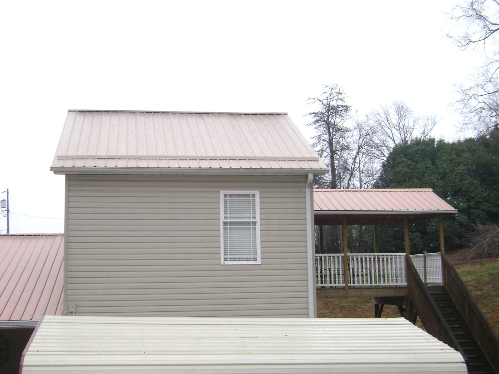 Tan metal roofs on a two story addition and attached porch, from a Roof Replacement job in Wrentham