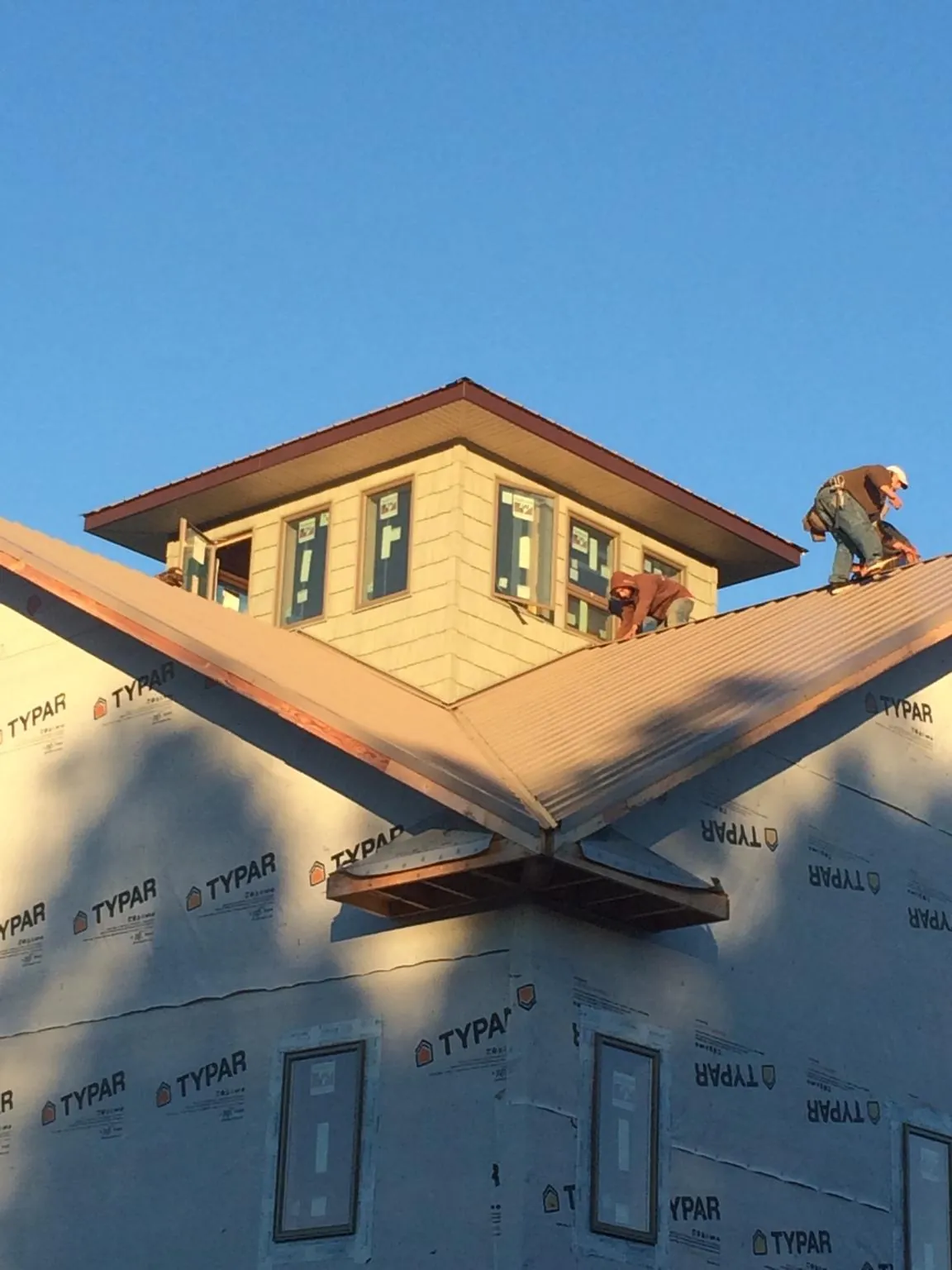 Roofers working around a rooftop cupola on a new metal roof at sunset — Roof Waterproofing in Wrentham by Roofing Brothers